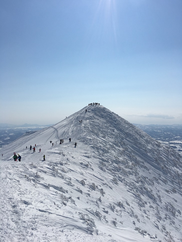 skiers and snowboarders hiking mt annupuri peak from grand hirafu
